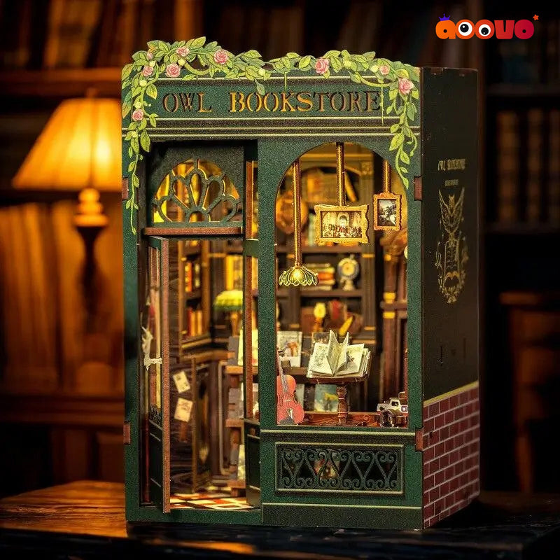 A miniature owl bookstore diorama model with intricate bookshelves, hanging lamps, and decorative floral arches, displayed on a wooden table with a warm, blurred library background.