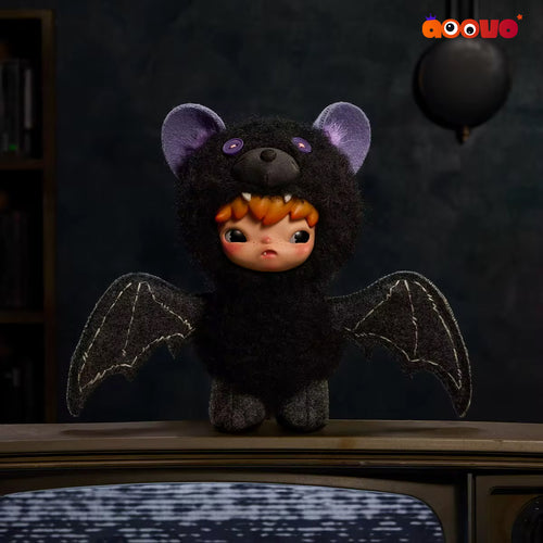 A cute, fuzzy bat-shaped doll with a black furry body, purple ears, orange hair, and outstretched wings, standing on top of a vintage television set against a dark, moody background.